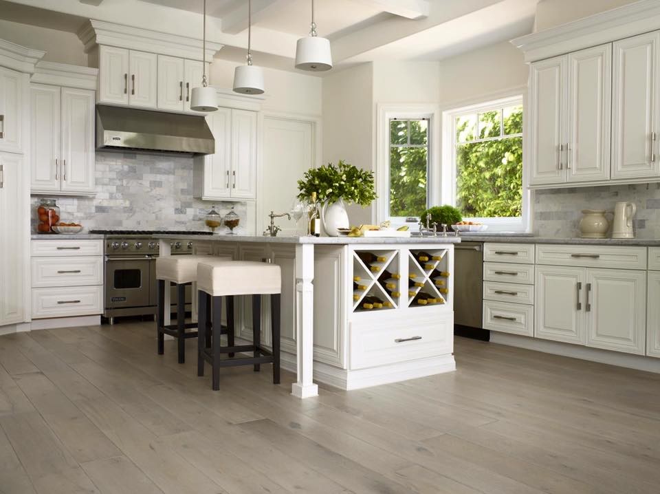 Example of a large transitional l-shaped light wood floor and brown floor kitchen design in Orange County with an undermount sink, raised-panel cabinets, white cabinets, quartzite countertops, gray backsplash, stone tile backsplash, stainless steel appliances and an island