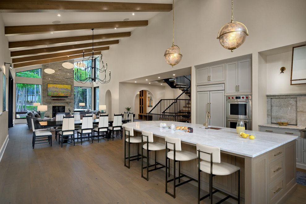 Open concept kitchen - huge transitional l-shaped medium tone wood floor, brown floor and exposed beam open concept kitchen idea with an undermount sink, recessed-panel cabinets, gray cabinets, quartzite countertops, multicolored backsplash, stone slab backsplash, stainless steel appliances, an island and white countertops