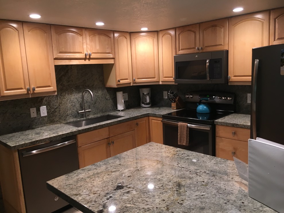 This is an example of a mid-sized transitional l-shaped kitchen in Hawaii with an undermount sink, raised-panel cabinets, beige cabinets, granite benchtops, green splashback, stone slab splashback, black appliances and with island.