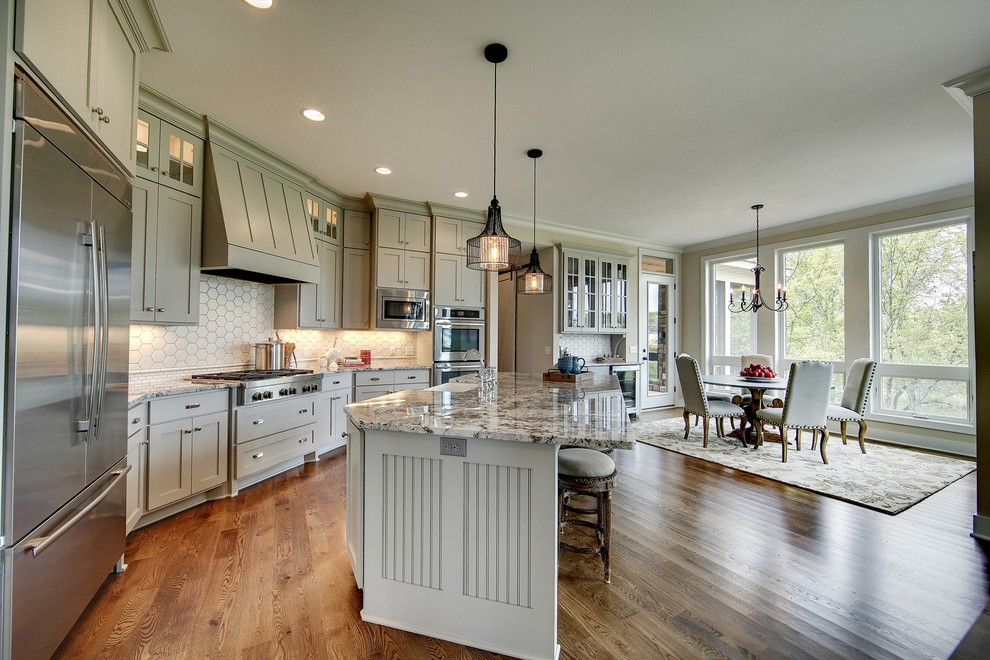 Inspiration for a large transitional single-wall eat-in kitchen in Minneapolis with a farmhouse sink, shaker cabinets, green cabinets, white splashback, ceramic splashback, stainless steel appliances, medium hardwood floors and with island.