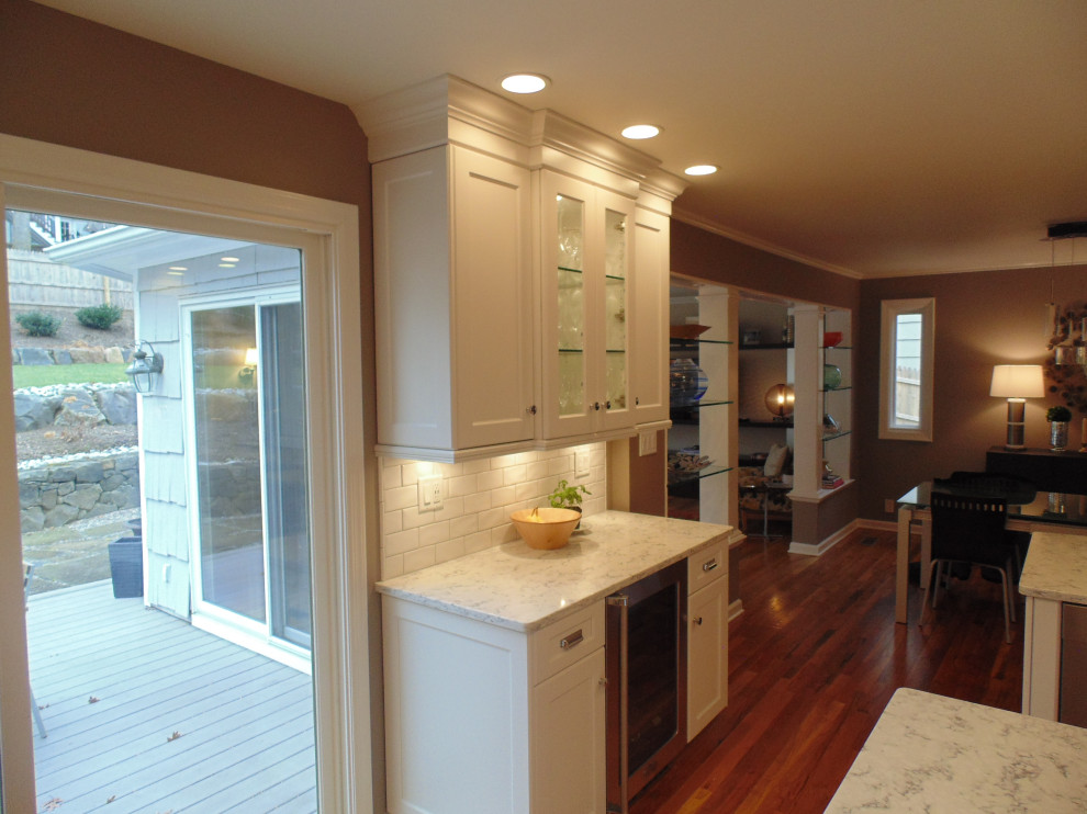 Large transitional u-shaped medium tone wood floor and brown floor eat-in kitchen photo with an undermount sink, recessed-panel cabinets, white cabinets, quartz countertops, white backsplash, subway tile backsplash, stainless steel appliances, an island and white countertops