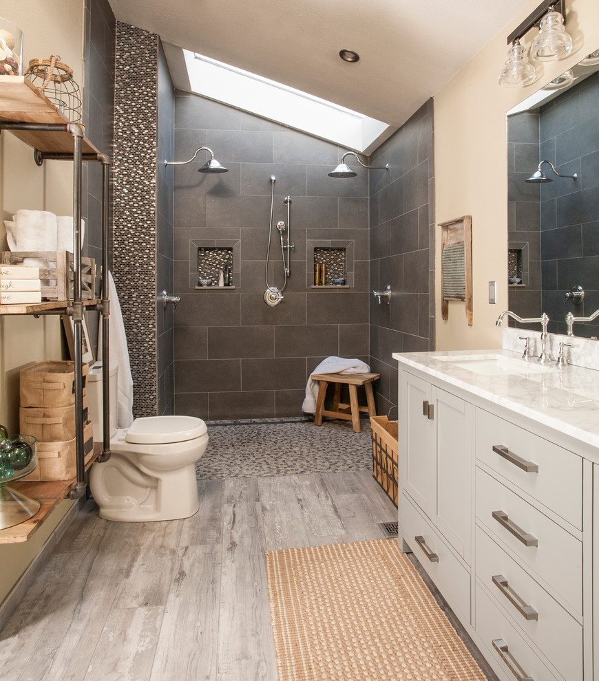 Photo of a mid-sized industrial master bathroom in Seattle with grey cabinets, a curbless shower, a two-piece toilet, gray tile, porcelain tile, beige walls, porcelain floors, a drop-in sink, marble benchtops, grey floor and shaker cabinets.