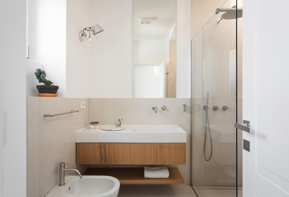 Пример оригинального дизайна: ванная комната среднего размера в стиле модернизм с светлыми деревянными фасадами, душем без бортиков, раздельным унитазом, бежевой плиткой, керамогранитной плиткой, белыми стенами, полом из керамогранита, душевой кабиной, раковиной с несколькими смесителями, бежевым полом, открытым душем, сиденьем для душа, тумбой под одну раковину и подвесной тумбой