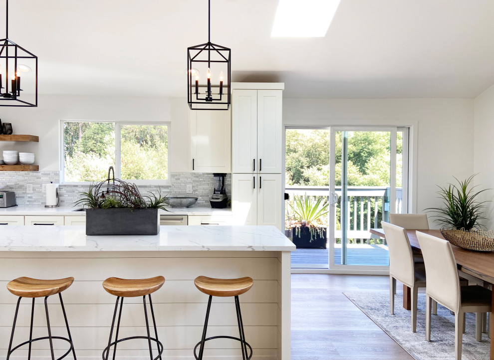 Inspiration for a mid-sized transitional l-shaped vinyl floor, brown floor and vaulted ceiling eat-in kitchen remodel with an undermount sink, shaker cabinets, white cabinets, quartz countertops, multicolored backsplash, mosaic tile backsplash, stainless steel appliances, an island and white countertops