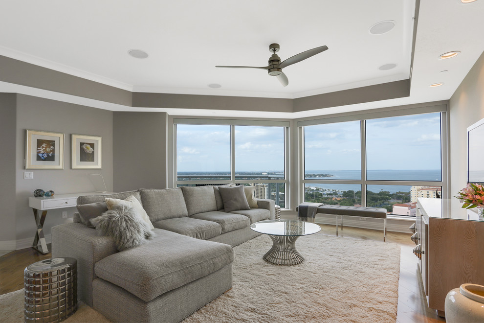 This is an example of a mid-sized contemporary formal open concept living room in Tampa with grey walls, medium hardwood floors, no fireplace, a freestanding tv and brown floor.