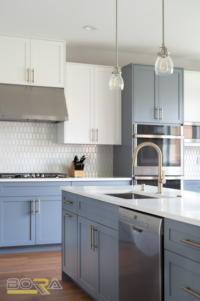 Example of a large transitional l-shaped medium tone wood floor and brown floor eat-in kitchen design in Seattle with an undermount sink, shaker cabinets, blue cabinets, quartz countertops, white backsplash, ceramic backsplash, stainless steel appliances, an island and white countertops