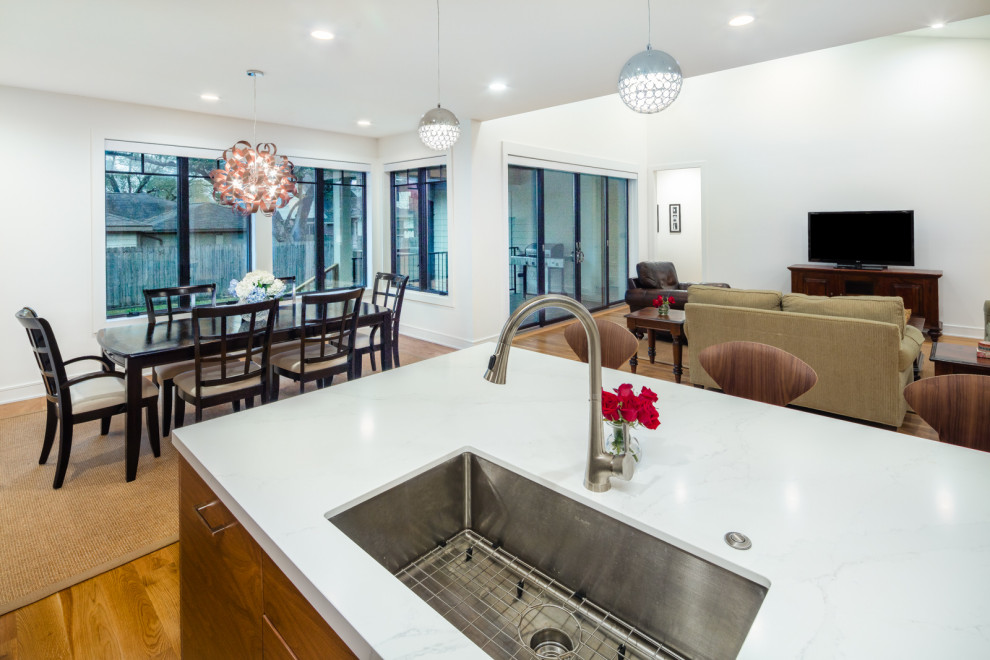 Mid-sized contemporary l-shaped eat-in kitchen in Houston with an undermount sink, flat-panel cabinets, medium wood cabinets, quartz benchtops, white splashback, engineered quartz splashback, stainless steel appliances, light hardwood floors, with island, multi-coloured floor and white benchtop.