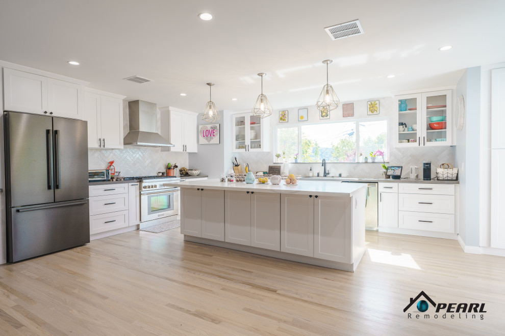 Large 1960s l-shaped light wood floor and beige floor eat-in kitchen photo in Los Angeles with a double-bowl sink, shaker cabinets, white cabinets, solid surface countertops, white backsplash, ceramic backsplash, stainless steel appliances, an island and gray countertops