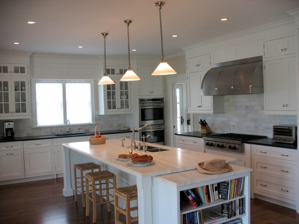 This is an example of a large beach style l-shaped kitchen in New York with an undermount sink, shaker cabinets, white cabinets, marble benchtops, white splashback, ceramic splashback, stainless steel appliances, dark hardwood floors and with island.