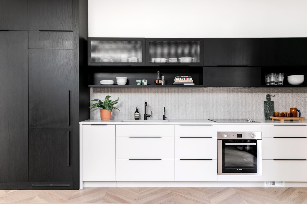 This is an example of a small contemporary galley open plan kitchen in Calgary with an undermount sink, flat-panel cabinets, white cabinets, quartzite benchtops, grey splashback, porcelain splashback, stainless steel appliances, light hardwood floors, no island, beige floor and white benchtop.