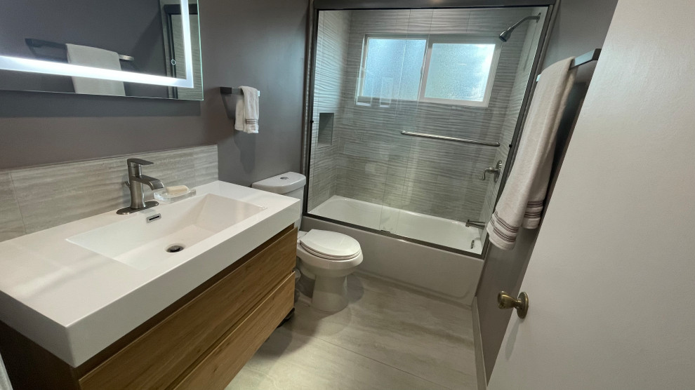 Drop-in bathtub - small modern gray tile and ceramic tile single-sink drop-in bathtub idea in Los Angeles with flat-panel cabinets, brown cabinets, a one-piece toilet, gray walls, quartz countertops and a floating vanity