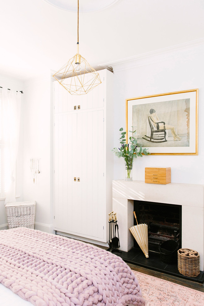 Photo of a mid-sized country master bedroom in London with white walls, dark hardwood floors, a standard fireplace, a stone fireplace surround and brown floor.