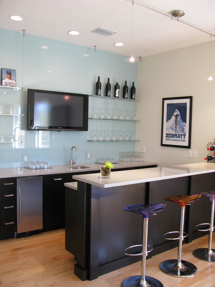 Photo of a contemporary galley seated home bar in Tampa with an undermount sink, flat-panel cabinets, black cabinets, blue splashback, glass sheet splashback and medium hardwood floors.
