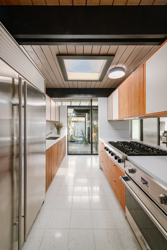 Mid-sized midcentury galley kitchen in Los Angeles with an undermount sink, flat-panel cabinets, medium wood cabinets, solid surface benchtops, no island, white floor, white benchtop and stainless steel appliances.