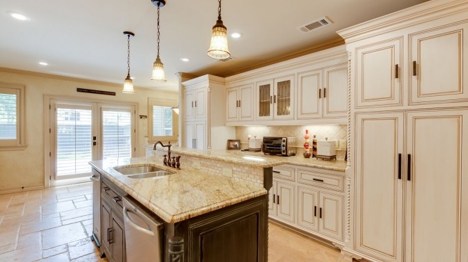 Mid-sized traditional galley open plan kitchen in Dallas with a double-bowl sink, raised-panel cabinets, white cabinets, granite benchtops, beige splashback, ceramic splashback, stainless steel appliances, ceramic floors, with island and beige floor.
