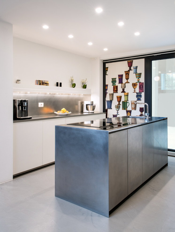 Mid-sized contemporary galley kitchen in Milan with an integrated sink, flat-panel cabinets, stainless steel cabinets, stainless steel benchtops, stainless steel appliances, concrete floors, with island, grey floor, grey splashback and grey benchtop.