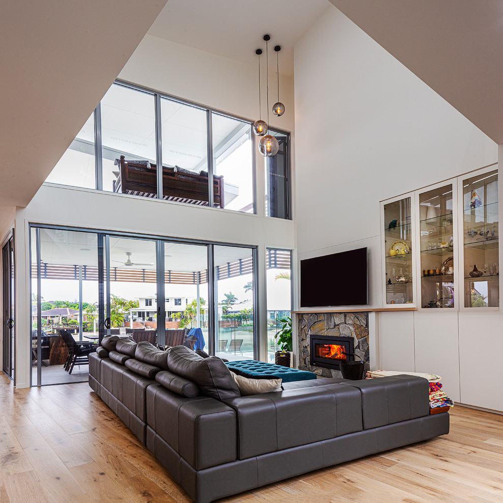 Design ideas for a contemporary open concept living room in Sunshine Coast with white walls, light hardwood floors, a standard fireplace, a stone fireplace surround, a wall-mounted tv and brown floor.