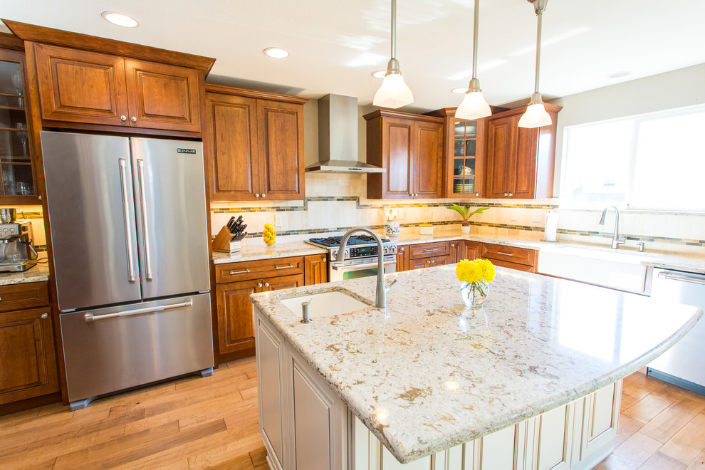 Large transitional l-shaped medium tone wood floor and brown floor eat-in kitchen photo in Denver with a farmhouse sink, raised-panel cabinets, medium tone wood cabinets, granite countertops, beige backsplash, stone tile backsplash, stainless steel appliances and an island