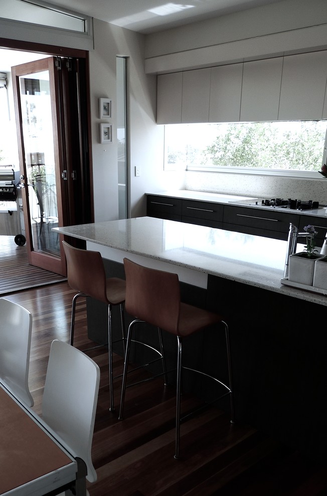 This is an example of a contemporary u-shaped eat-in kitchen in Brisbane with an undermount sink, flat-panel cabinets, dark wood cabinets, quartz benchtops, stone slab splashback and stainless steel appliances.