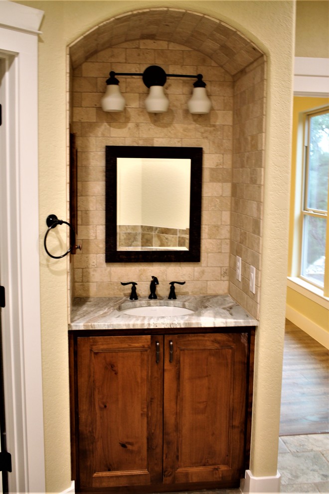 Photo of a mid-sized country master bathroom in Other with raised-panel cabinets, dark wood cabinets, beige tile, travertine, beige walls, porcelain floors, an undermount sink, granite benchtops, brown floor and multi-coloured benchtops.