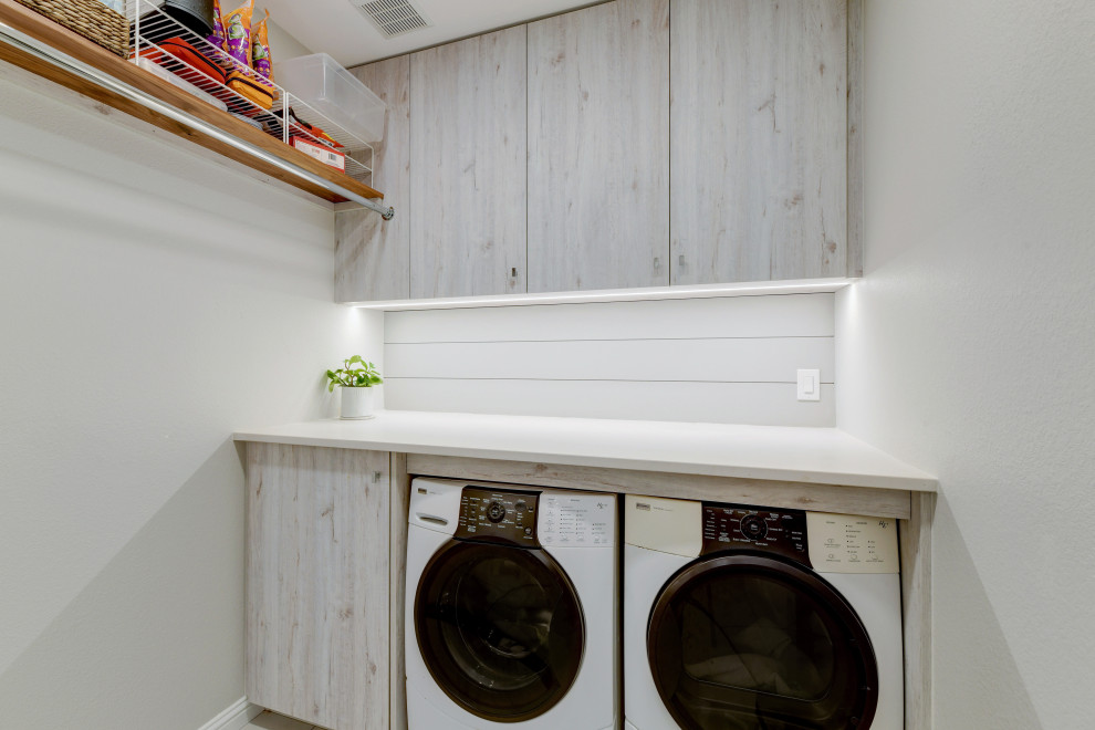 Photo of a mid-sized transitional galley dedicated laundry room in Austin with an undermount sink, flat-panel cabinets, light wood cabinets, quartz benchtops, grey splashback, timber splashback, grey walls, ceramic floors, a side-by-side washer and dryer, grey floor, grey benchtop and planked wall panelling.