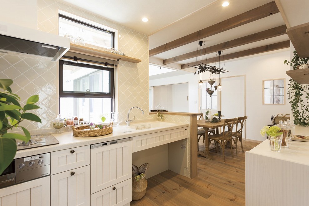 This is an example of a traditional single-wall open plan kitchen in Other with an integrated sink, shaker cabinets, white cabinets, beige splashback, medium hardwood floors, a peninsula, brown floor and white benchtop.
