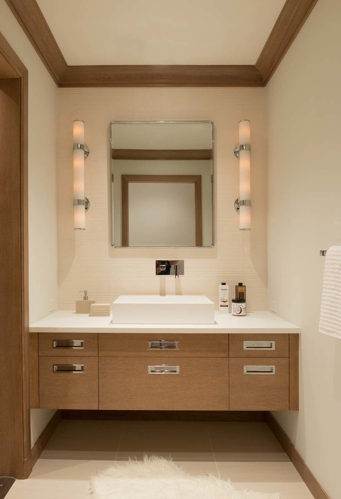This is an example of a contemporary powder room in New York with flat-panel cabinets, light wood cabinets, beige walls, a vessel sink and beige floor.