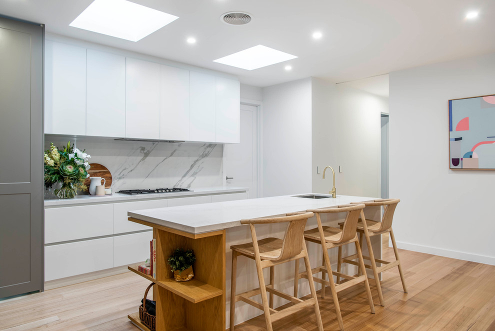 Inspiration for a contemporary l-shaped kitchen in Canberra - Queanbeyan with an undermount sink, quartz benchtops, white splashback, stone slab splashback, light hardwood floors, with island, flat-panel cabinets, white cabinets, panelled appliances, beige floor and white benchtop.