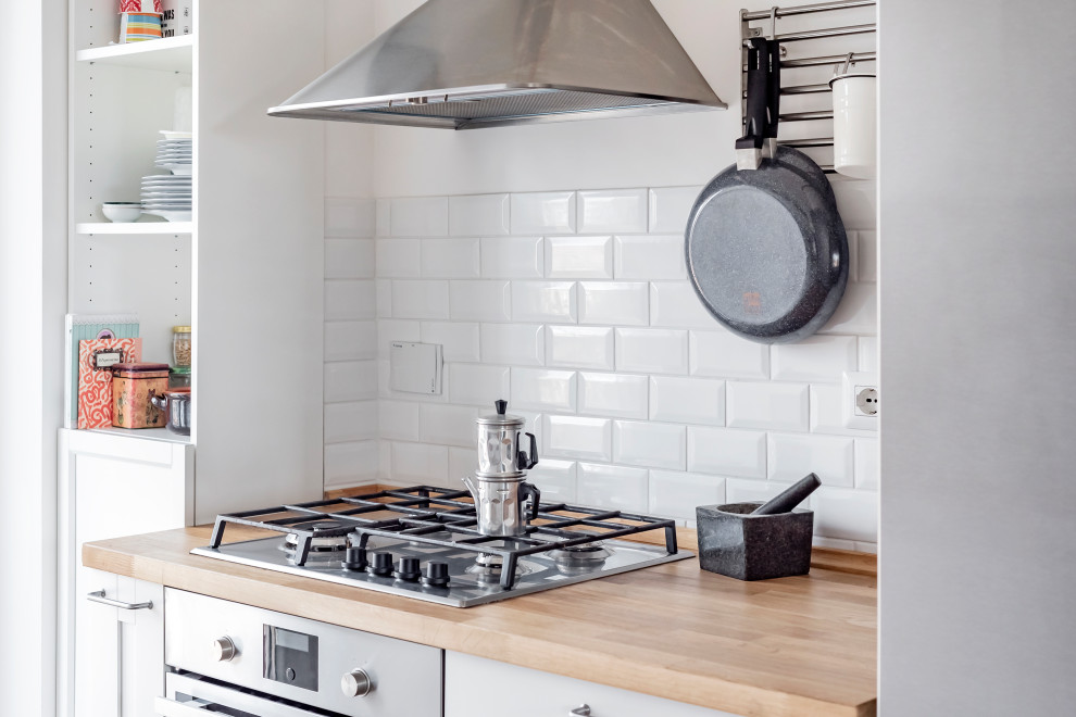 Inspiration for a small scandinavian galley open plan kitchen in Rome with a double-bowl sink, flat-panel cabinets, white cabinets, wood benchtops, white splashback, ceramic splashback, stainless steel appliances, light hardwood floors and no island.