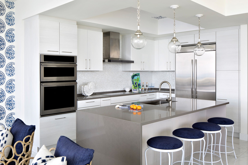 Inspiration for a beach style l-shaped open plan kitchen in Miami with an undermount sink, flat-panel cabinets, white cabinets, white splashback, stainless steel appliances, with island and white floor.
