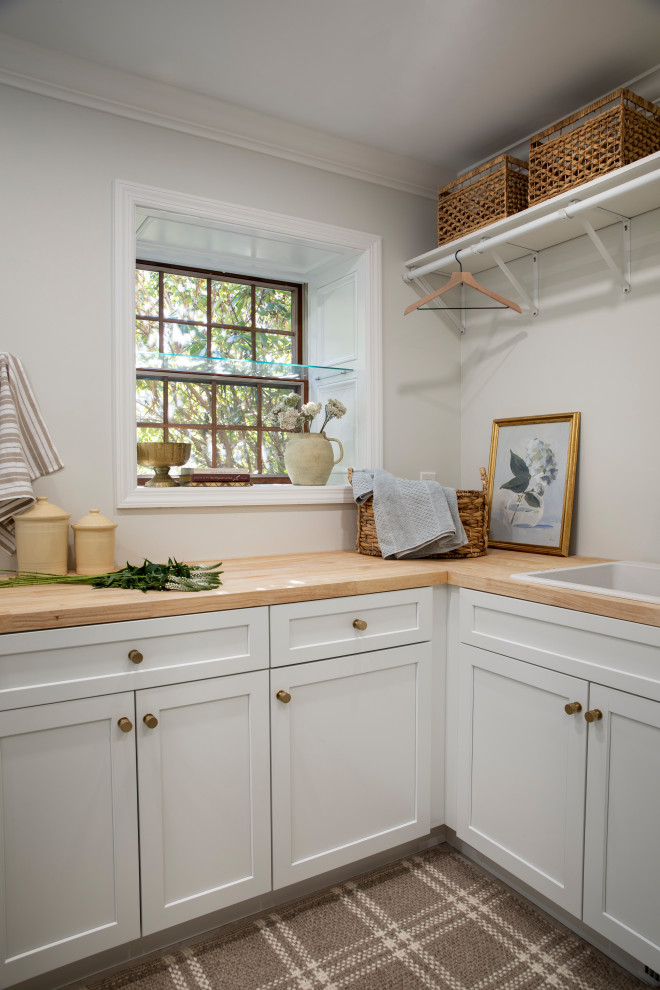 Beach style l-shaped utility room in Other with a drop-in sink, recessed-panel cabinets, white cabinets, wood benchtops, white walls and carpet.