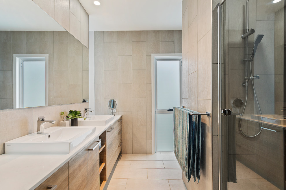 This is an example of a large modern master bathroom in Brisbane with light wood cabinets, beige tile, ceramic tile, beige walls, an alcove shower, ceramic floors, an integrated sink, beige floor, a hinged shower door, furniture-like cabinets, a freestanding tub, a two-piece toilet and engineered quartz benchtops.