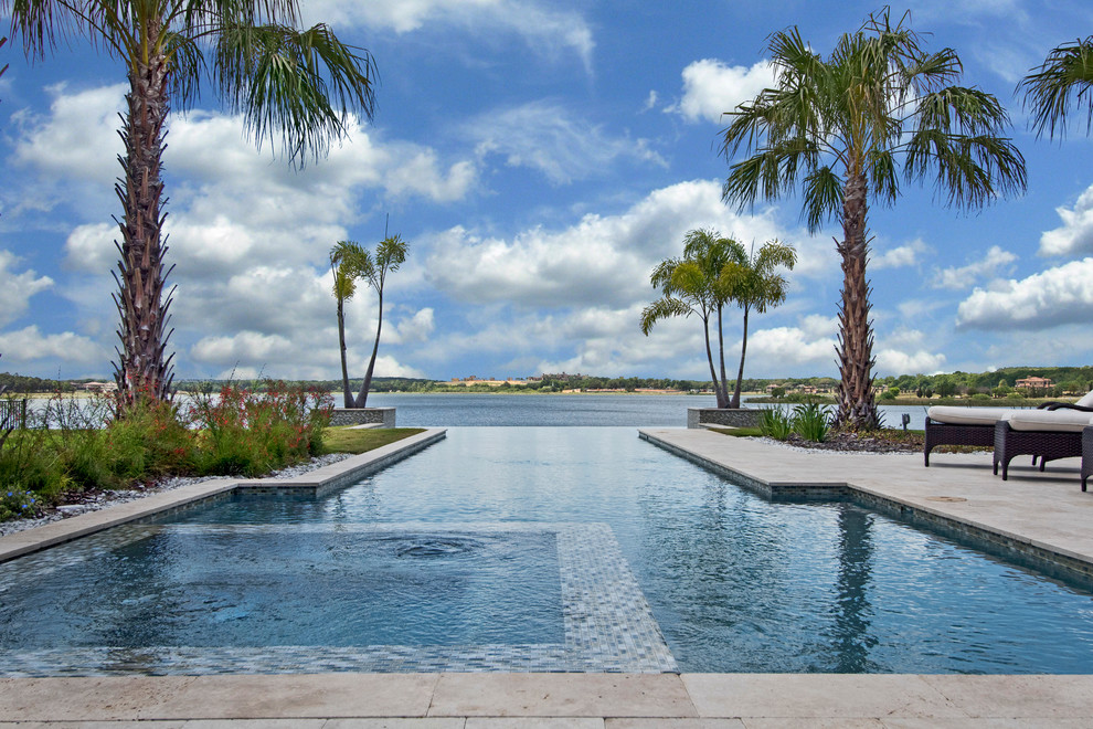 Traditional backyard custom-shaped infinity pool in Tampa with a hot tub and natural stone pavers.