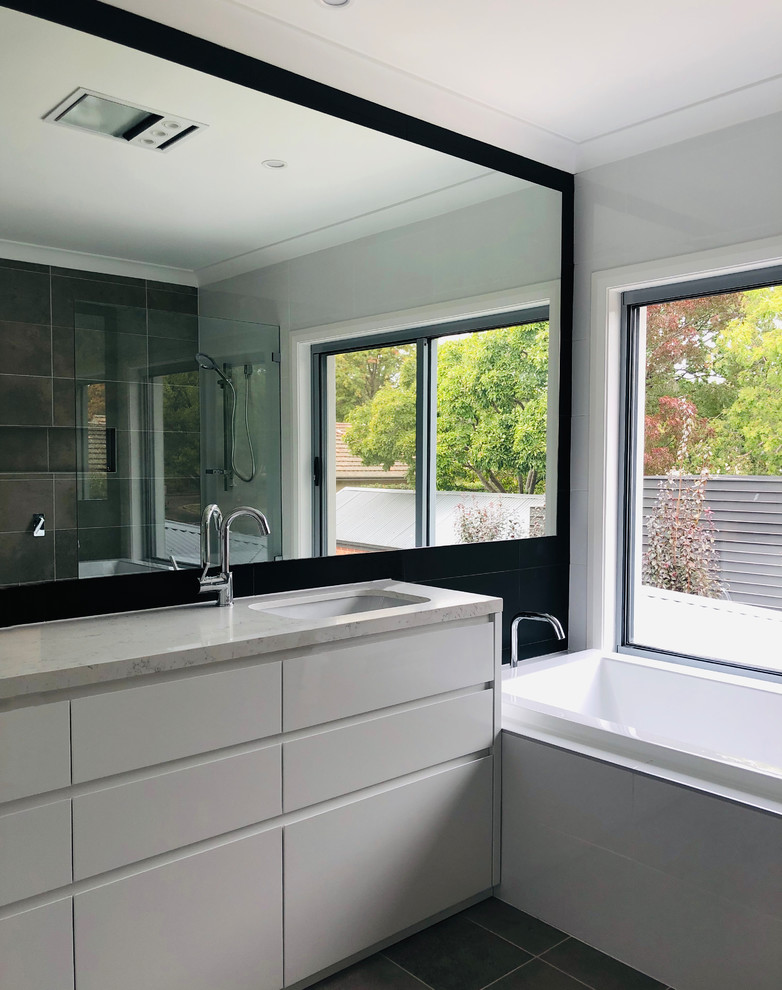 This is an example of a mid-sized contemporary master wet room bathroom in Canberra - Queanbeyan with flat-panel cabinets, white cabinets, a drop-in tub, multi-coloured tile, porcelain tile, multi-coloured walls, porcelain floors, a drop-in sink, marble benchtops, grey floor, an open shower and multi-coloured benchtops.