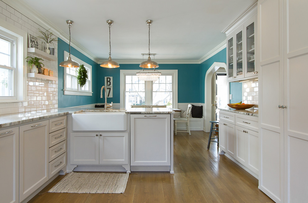 Inspiration for a mid-sized transitional u-shaped light wood floor and brown floor eat-in kitchen remodel in Tampa with a farmhouse sink, recessed-panel cabinets, white cabinets, granite countertops, white backsplash, subway tile backsplash, stainless steel appliances and a peninsula