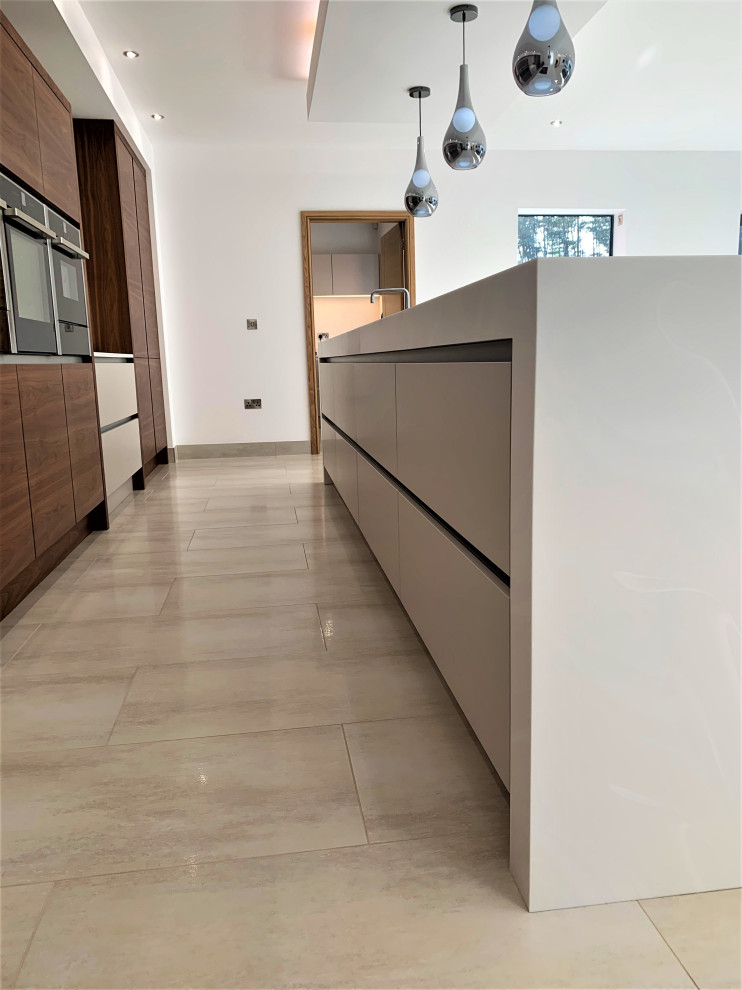 Inspiration for a large traditional single-wall kitchen in Other with an integrated sink, flat-panel cabinets, medium wood cabinets, solid surface benchtops, glass sheet splashback, black appliances, porcelain floors, with island and white benchtop.