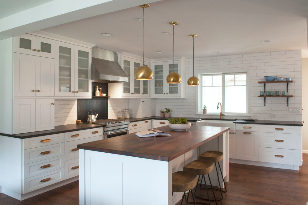 This is an example of a large country l-shaped eat-in kitchen in Burlington with a farmhouse sink, recessed-panel cabinets, white cabinets, limestone benchtops, white splashback, subway tile splashback, stainless steel appliances, dark hardwood floors and with island.