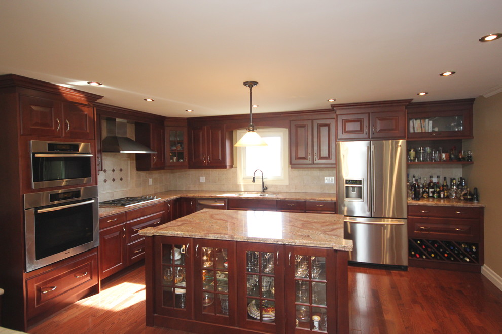 Photo of a mid-sized transitional l-shaped separate kitchen in Toronto with beige splashback, stone slab splashback, stainless steel appliances, with island, a double-bowl sink, raised-panel cabinets, medium hardwood floors and dark wood cabinets.