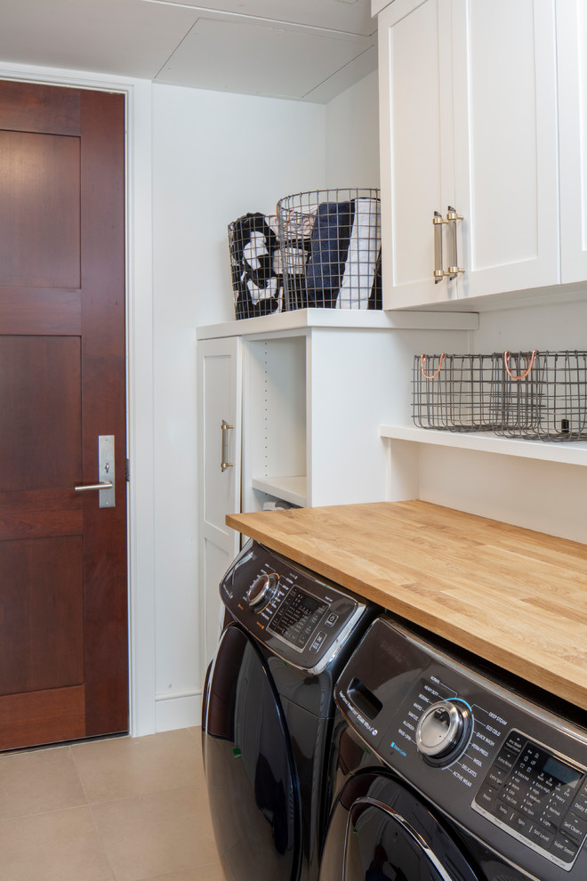 This is an example of a mid-sized modern single-wall dedicated laundry room in Austin with shaker cabinets, white cabinets, wood benchtops, white walls, ceramic floors and a side-by-side washer and dryer.