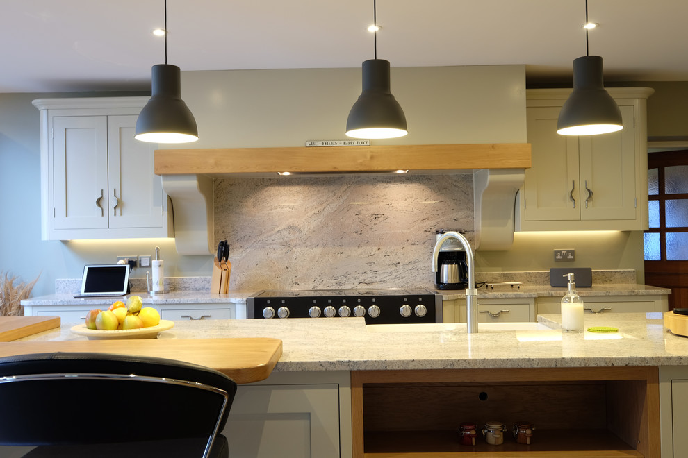 Large contemporary l-shaped open plan kitchen in Surrey with a farmhouse sink, shaker cabinets, green cabinets, granite benchtops, multi-coloured splashback, stone slab splashback, stainless steel appliances, porcelain floors, with island, multi-coloured floor and grey benchtop.