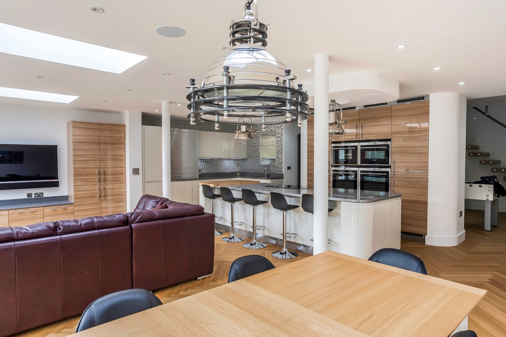 Large contemporary open plan kitchen in Essex with an undermount sink, flat-panel cabinets, white cabinets, quartzite benchtops, metallic splashback, metal splashback, black appliances, light hardwood floors and with island.