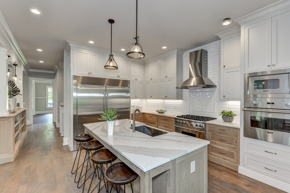 This is an example of a transitional l-shaped kitchen in Atlanta with a farmhouse sink, beaded inset cabinets, light wood cabinets, quartz benchtops, white splashback, ceramic splashback, stainless steel appliances, medium hardwood floors and with island.