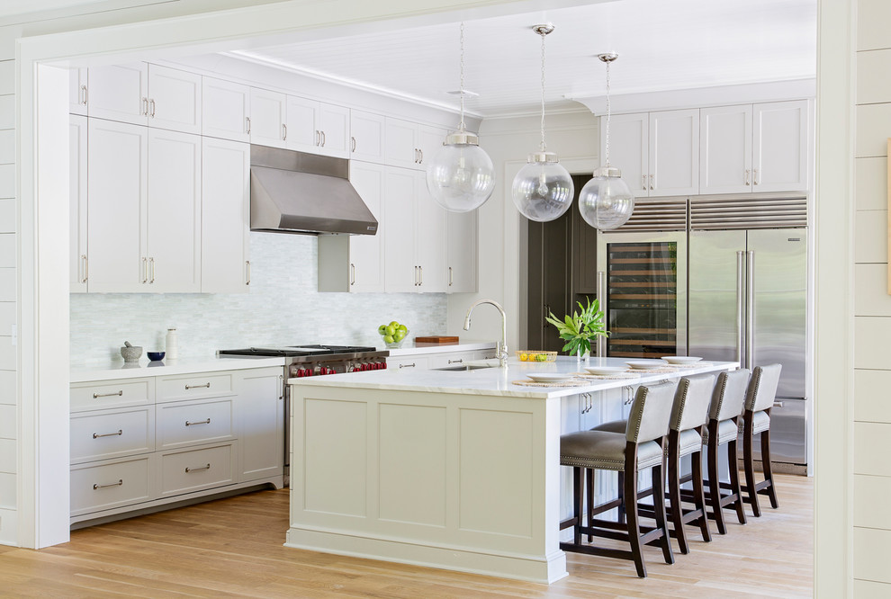 Beach style l-shaped kitchen in Charleston with an undermount sink, shaker cabinets, white cabinets, white splashback, stainless steel appliances, medium hardwood floors, with island and brown floor.