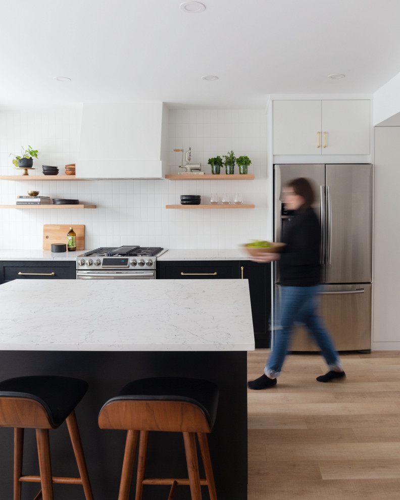 Inspiration for a mid-sized modern l-shaped open plan kitchen in Calgary with an undermount sink, shaker cabinets, black cabinets, quartz benchtops, white splashback, porcelain splashback, stainless steel appliances, light hardwood floors, with island, brown floor and white benchtop.