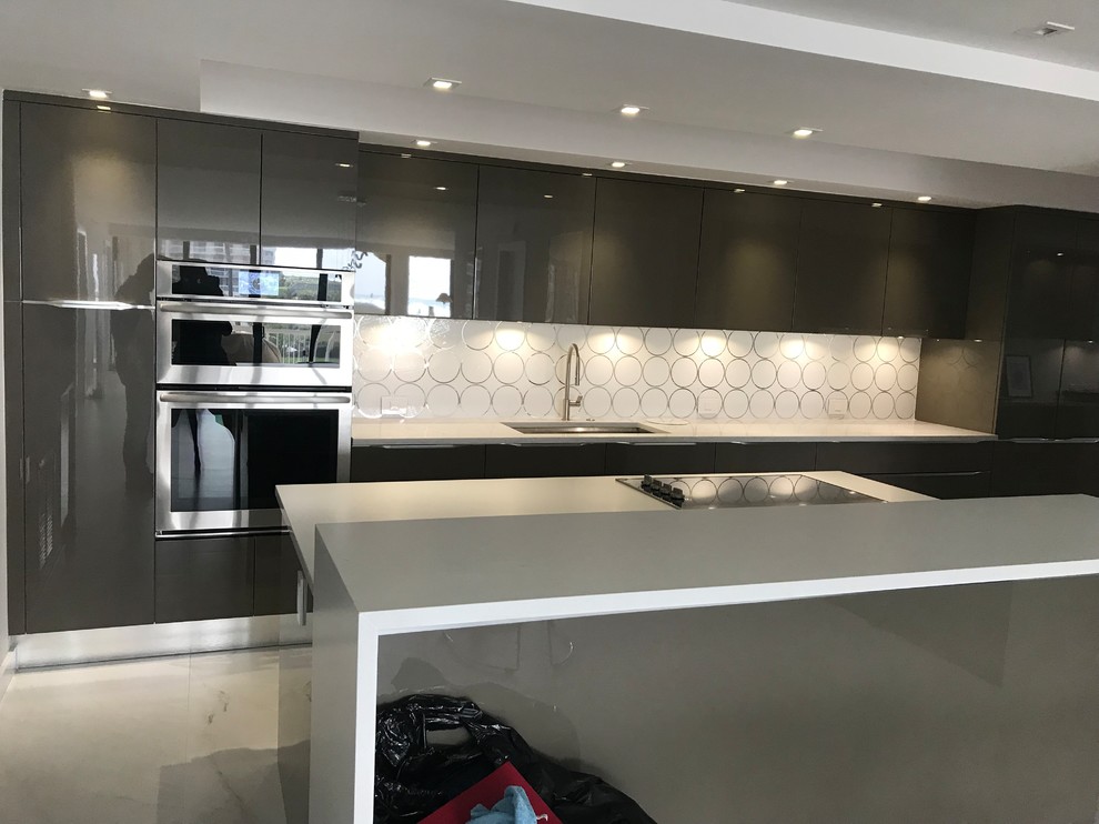 Photo of a mid-sized contemporary kitchen in Miami with an undermount sink, flat-panel cabinets, green cabinets, quartz benchtops, white splashback, glass tile splashback, panelled appliances, porcelain floors, with island, white floor and white benchtop.