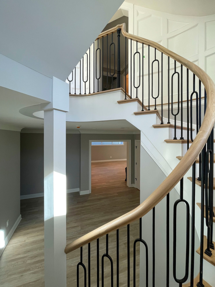 Стильный дизайн: огромная изогнутая деревянная лестница в стиле неоклассика (современная классика) с деревянными ступенями, перилами из смешанных материалов и панелями на стенах - последний тренд