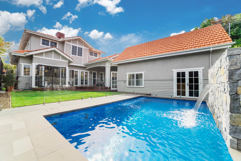 Photo of a mid-sized traditional backyard rectangular natural pool in Melbourne with a water feature and natural stone pavers.