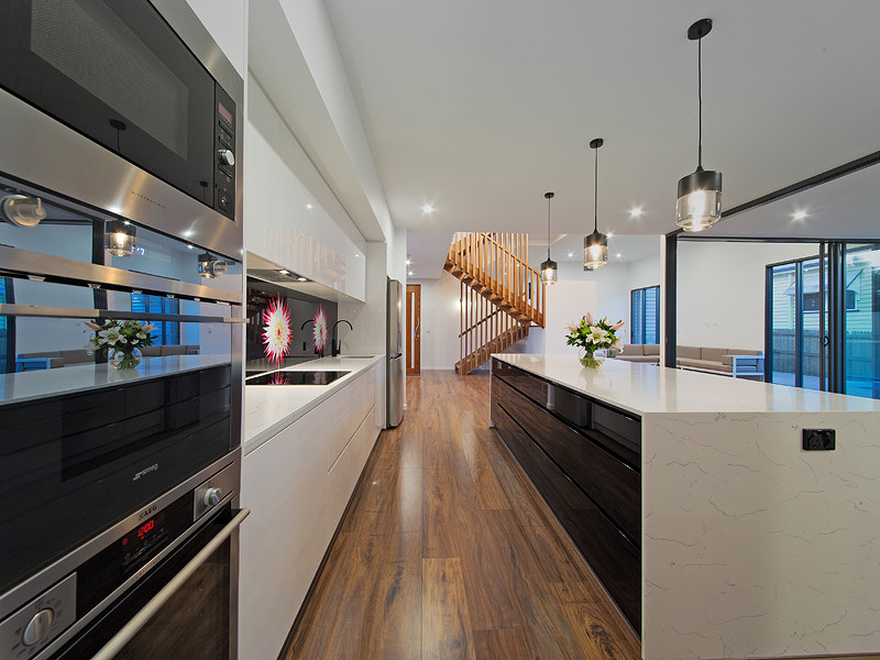 Large transitional kitchen in Brisbane with an undermount sink, beaded inset cabinets, black cabinets, granite benchtops, black splashback, glass sheet splashback, stainless steel appliances, medium hardwood floors, with island, brown floor and white benchtop.
