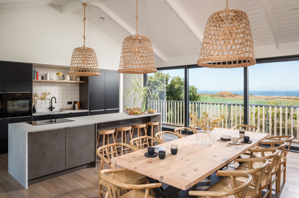 Photo of an expansive nautical open plan kitchen with a built-in sink, flat-panel cabinets, black cabinets, concrete worktops, white splashback, porcelain splashback, integrated appliances, light hardwood flooring, an island, brown floors, grey worktops, a vaulted ceiling and a feature wall.