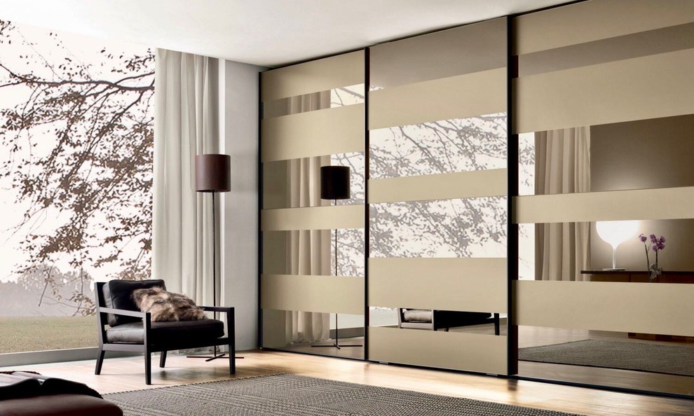 This is an example of a large contemporary gender-neutral built-in wardrobe in Miami with glass-front cabinets, light hardwood floors and beige floor.